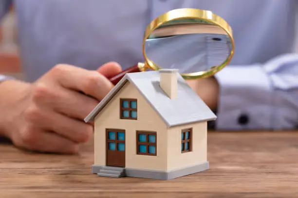 Expert immobilier examinant une maison miniature avec une loupe pour estimer son prix de vente